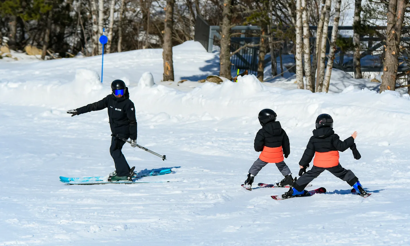 monitor esquiando de espaldas delante de dos niños debutantes en cuña en Baqueira Beret — Alpine Ski Academy