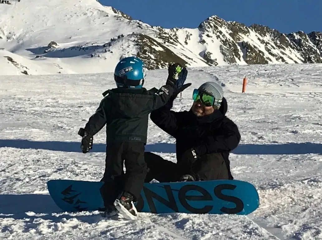 Cours de snowboard pour débutants avec Alpine Ski Academy à Baqueira : un enfant tape dans la main de son moniteur à côté de la planche